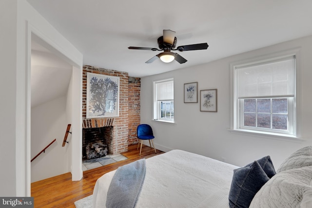 bedroom with a brick fireplace, wood finished floors, and a ceiling fan