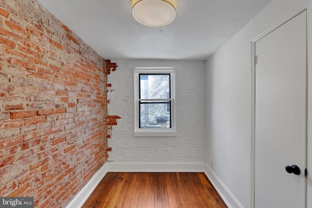 unfurnished room with brick wall, baseboards, and hardwood / wood-style floors