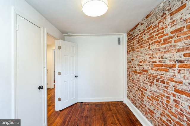 hallway featuring visible vents, baseboards, brick wall, and dark wood finished floors