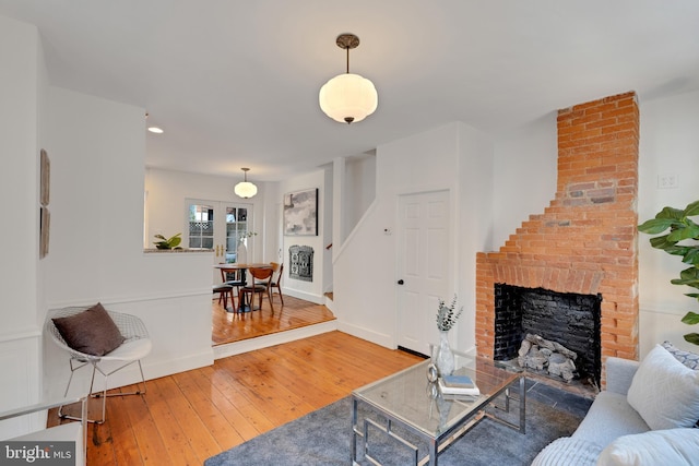 living area with a wainscoted wall, a brick fireplace, and wood-type flooring