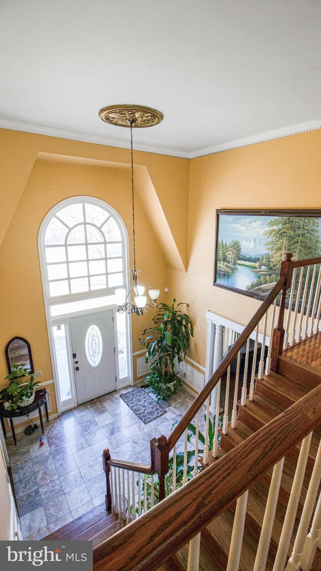 foyer entrance with stairway, crown molding, and an inviting chandelier