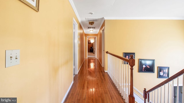 hallway featuring hardwood / wood-style floors, baseboards, visible vents, crown molding, and an upstairs landing