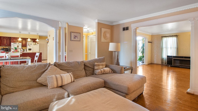 living area with crown molding, decorative columns, wood finished floors, and visible vents