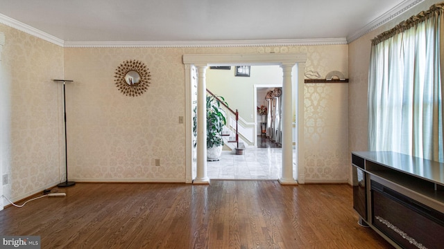 unfurnished dining area featuring wood finished floors, ornamental molding, wallpapered walls, and decorative columns