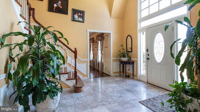 entrance foyer with stairway, a high ceiling, and a wainscoted wall