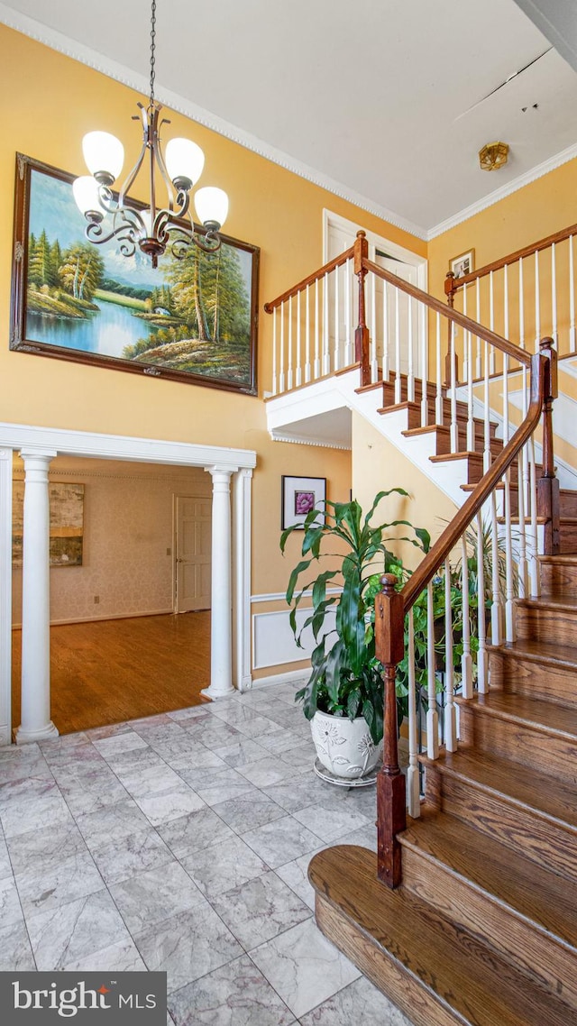 entrance foyer featuring a chandelier, marble finish floor, ornate columns, and ornamental molding