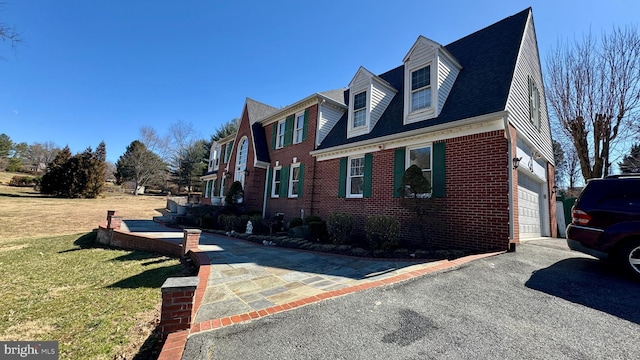 view of property exterior featuring a garage, a lawn, brick siding, and driveway