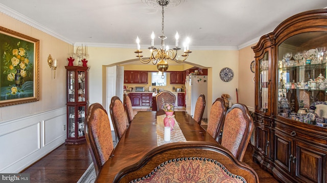 dining space featuring arched walkways, a notable chandelier, a wainscoted wall, and ornamental molding