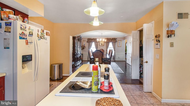 kitchen with visible vents, decorative light fixtures, white refrigerator with ice dispenser, arched walkways, and light countertops