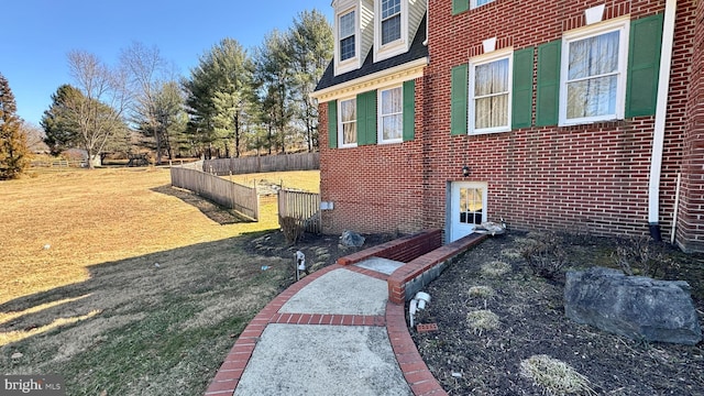 view of property exterior with a yard, fence, and brick siding