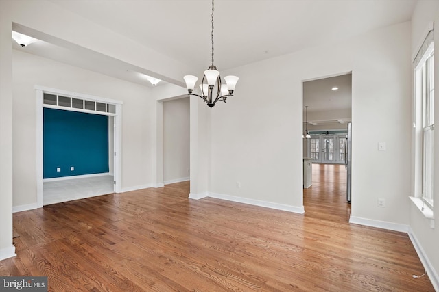 unfurnished dining area featuring a wealth of natural light, baseboards, a chandelier, and wood finished floors