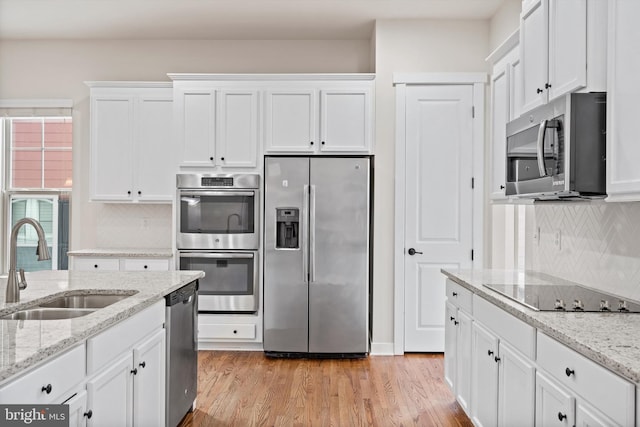 kitchen with a sink, white cabinets, light wood-style floors, appliances with stainless steel finishes, and tasteful backsplash