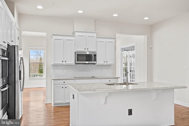 kitchen featuring stainless steel appliances, light wood finished floors, a sink, and white cabinetry