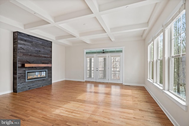 unfurnished living room featuring light wood finished floors, a glass covered fireplace, a wealth of natural light, and baseboards