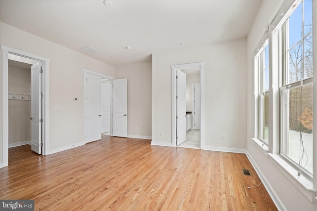 unfurnished bedroom with a walk in closet, light wood finished floors, visible vents, connected bathroom, and baseboards