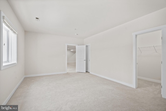 unfurnished bedroom with light carpet, a spacious closet, visible vents, and a closet