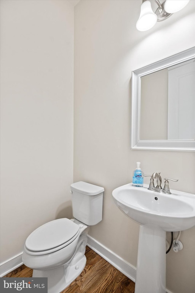 half bathroom with toilet, baseboards, and wood finished floors