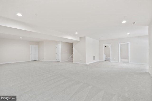 finished basement with light carpet, visible vents, baseboards, stairs, and recessed lighting