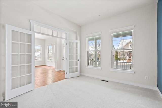 carpeted empty room featuring a healthy amount of sunlight, baseboards, visible vents, and french doors