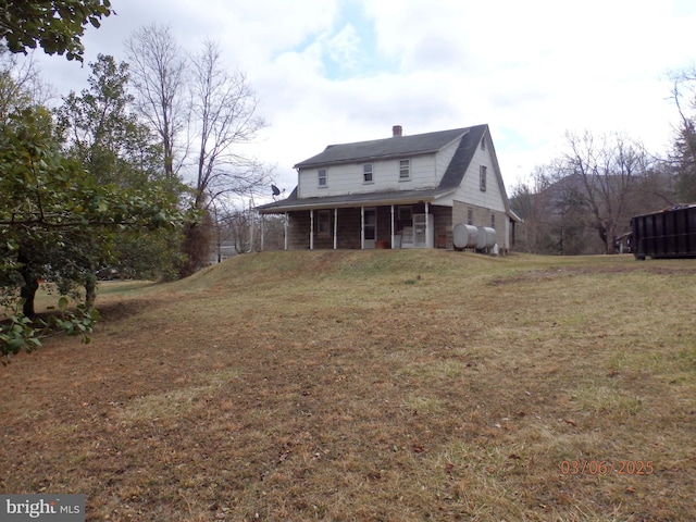 rear view of house featuring a yard, covered porch, and a chimney