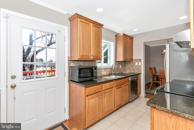 kitchen with a sink, stainless steel appliances, backsplash, and dark stone counters