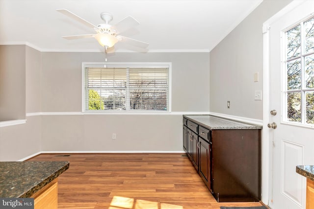 kitchen featuring a ceiling fan, baseboards, dark stone counters, light wood-style flooring, and ornamental molding