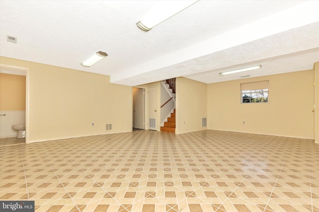 basement featuring stairway, a textured ceiling, and visible vents