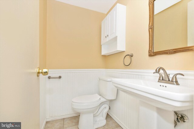 half bath featuring tile patterned flooring, wainscoting, toilet, and a sink