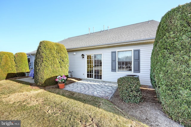 back of property with roof with shingles, a patio, and a yard