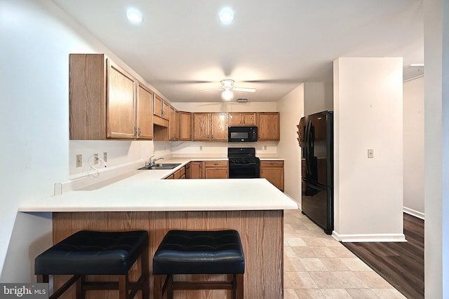 kitchen with light countertops, a ceiling fan, a sink, a peninsula, and black appliances