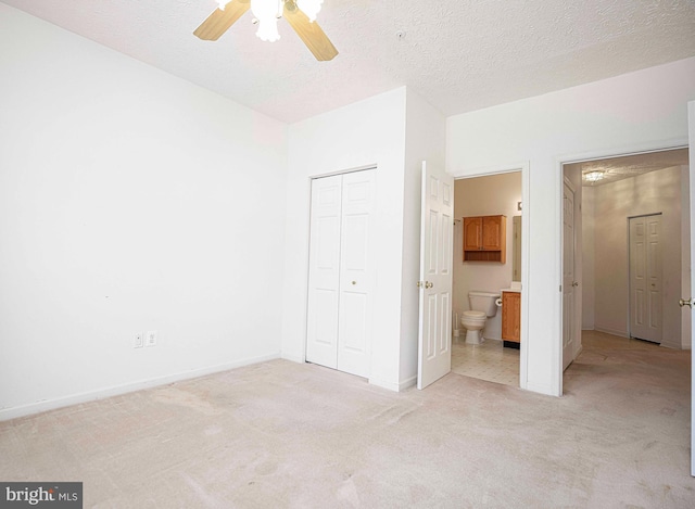 unfurnished bedroom with a textured ceiling, ensuite bath, a closet, baseboards, and light colored carpet