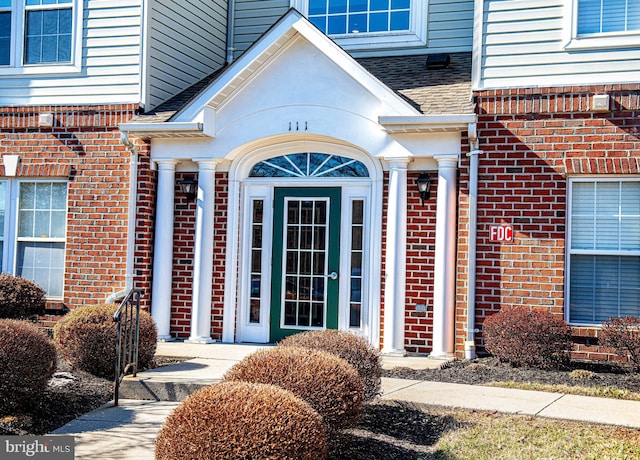 view of exterior entry featuring brick siding and roof with shingles