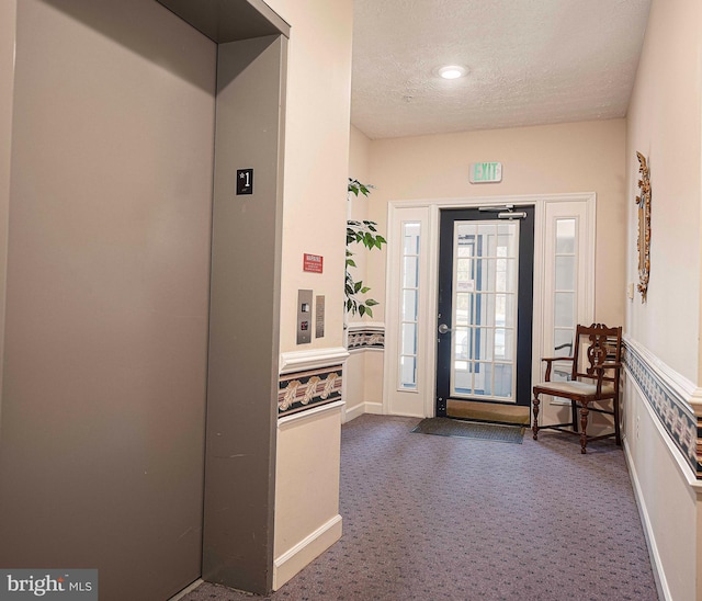 foyer with elevator, baseboards, dark colored carpet, and a textured ceiling