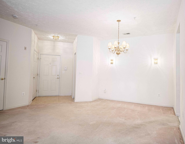 empty room with a textured ceiling, an inviting chandelier, baseboards, and light carpet