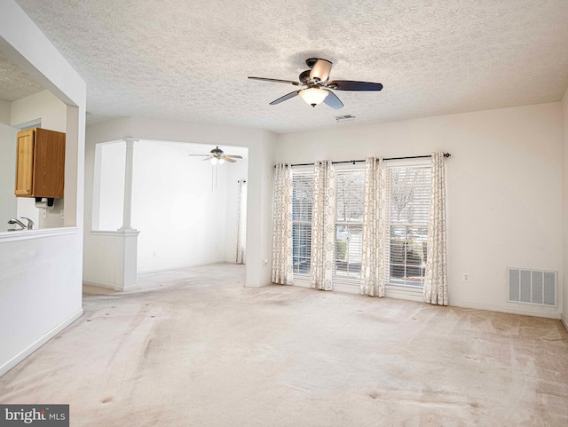 unfurnished room with visible vents, light colored carpet, a ceiling fan, and decorative columns