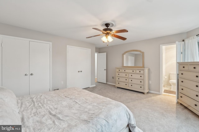 bedroom with two closets, ensuite bathroom, a ceiling fan, light carpet, and baseboards