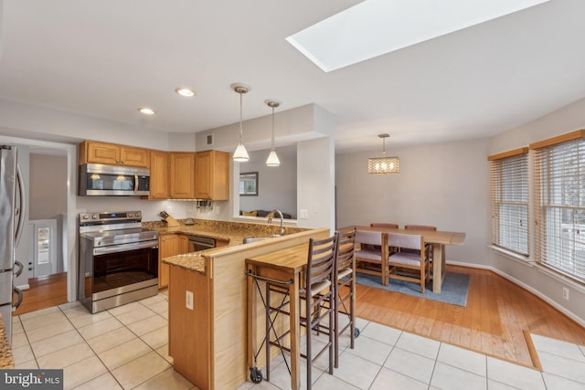 kitchen featuring a peninsula, a breakfast bar, a sink, appliances with stainless steel finishes, and decorative light fixtures