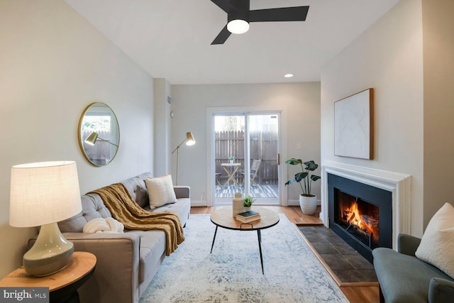 living area with dark wood-style flooring, a fireplace with flush hearth, and a ceiling fan