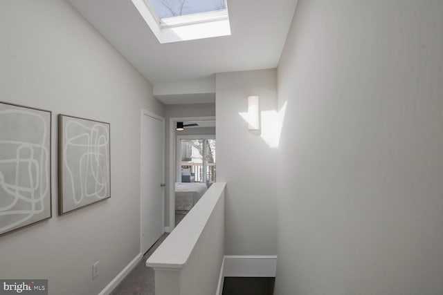 hall with a skylight, baseboards, and an upstairs landing