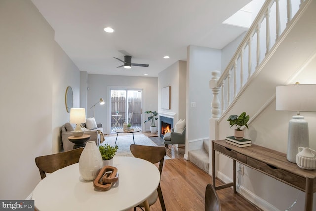 dining room with a warm lit fireplace, ceiling fan, wood finished floors, stairs, and recessed lighting