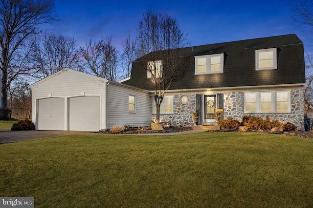 colonial inspired home with driveway, a garage, a shingled roof, stone siding, and a front lawn