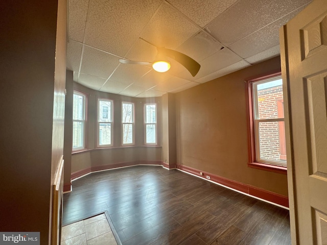 empty room with a drop ceiling, ceiling fan, baseboards, and wood finished floors