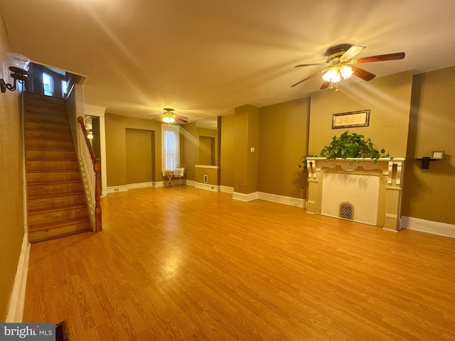 unfurnished living room with a ceiling fan, baseboards, stairway, and wood finished floors