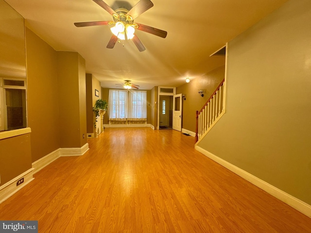 unfurnished living room featuring wood finished floors, visible vents, baseboards, and stairs