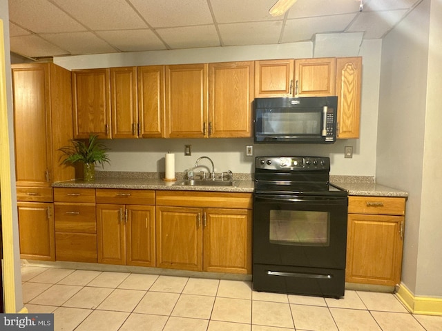 kitchen with light tile patterned floors, brown cabinetry, a sink, a drop ceiling, and black appliances