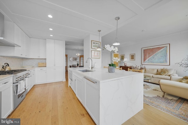 kitchen with open floor plan, stainless steel stove, light wood-type flooring, wall chimney range hood, and a sink