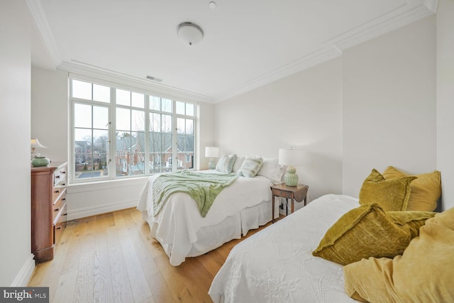 bedroom with ornamental molding, visible vents, light wood-style flooring, and baseboards