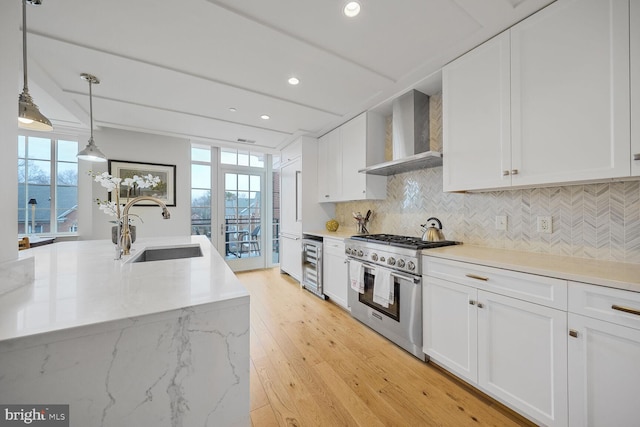 kitchen with beverage cooler, a sink, high end range, wall chimney exhaust hood, and tasteful backsplash