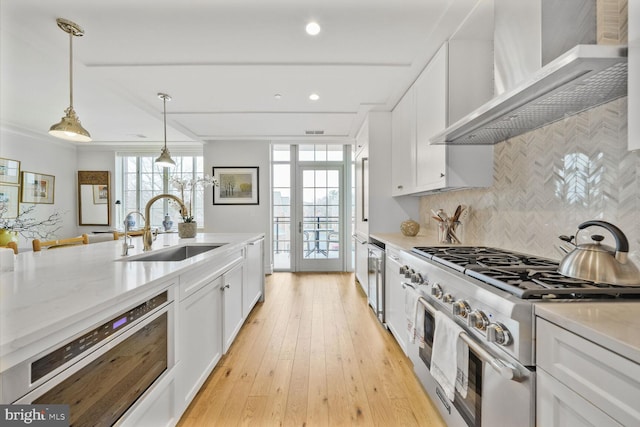 kitchen with tasteful backsplash, appliances with stainless steel finishes, white cabinetry, a sink, and wall chimney range hood