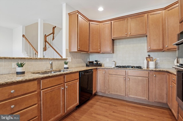 kitchen with dishwasher, light stone countertops, light wood-type flooring, gas stovetop, and a sink